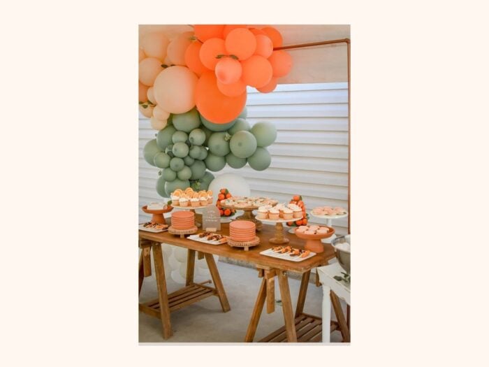 Little Cutie baby shower ideas with citrus balloons, cake table, and orange themed decor

