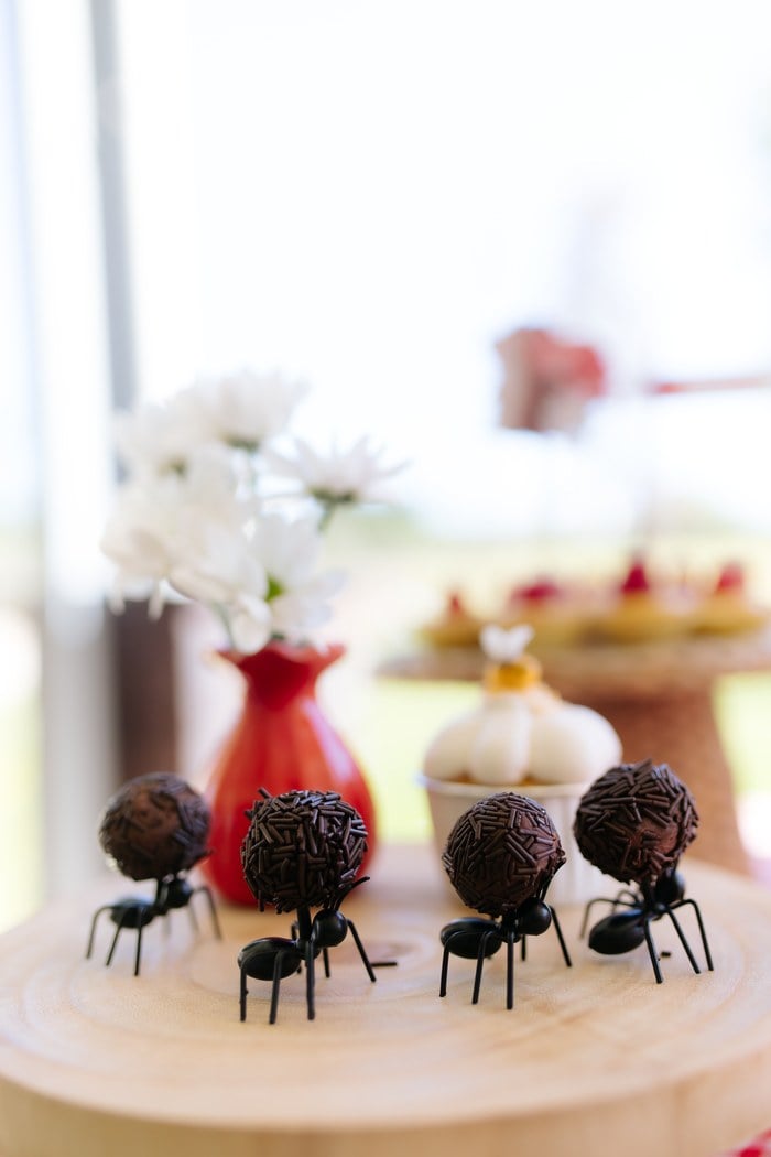 Chocolate sprinkle cake pops carried by tiny ant decorations on a wood stand