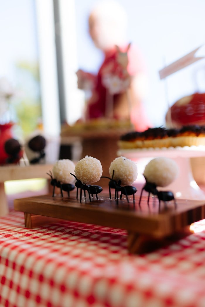 White coconut cake pops carried by tiny ant decorations on a wooden tray