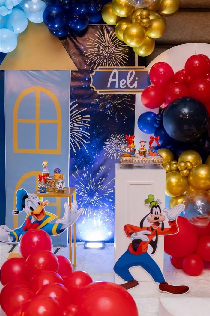 Minnie Mouse birthday cake beside a castle backdrop and balloon garland