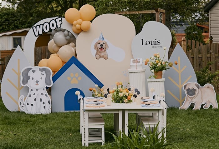 Puppy party backdrop with a blue dog house and styled children's table